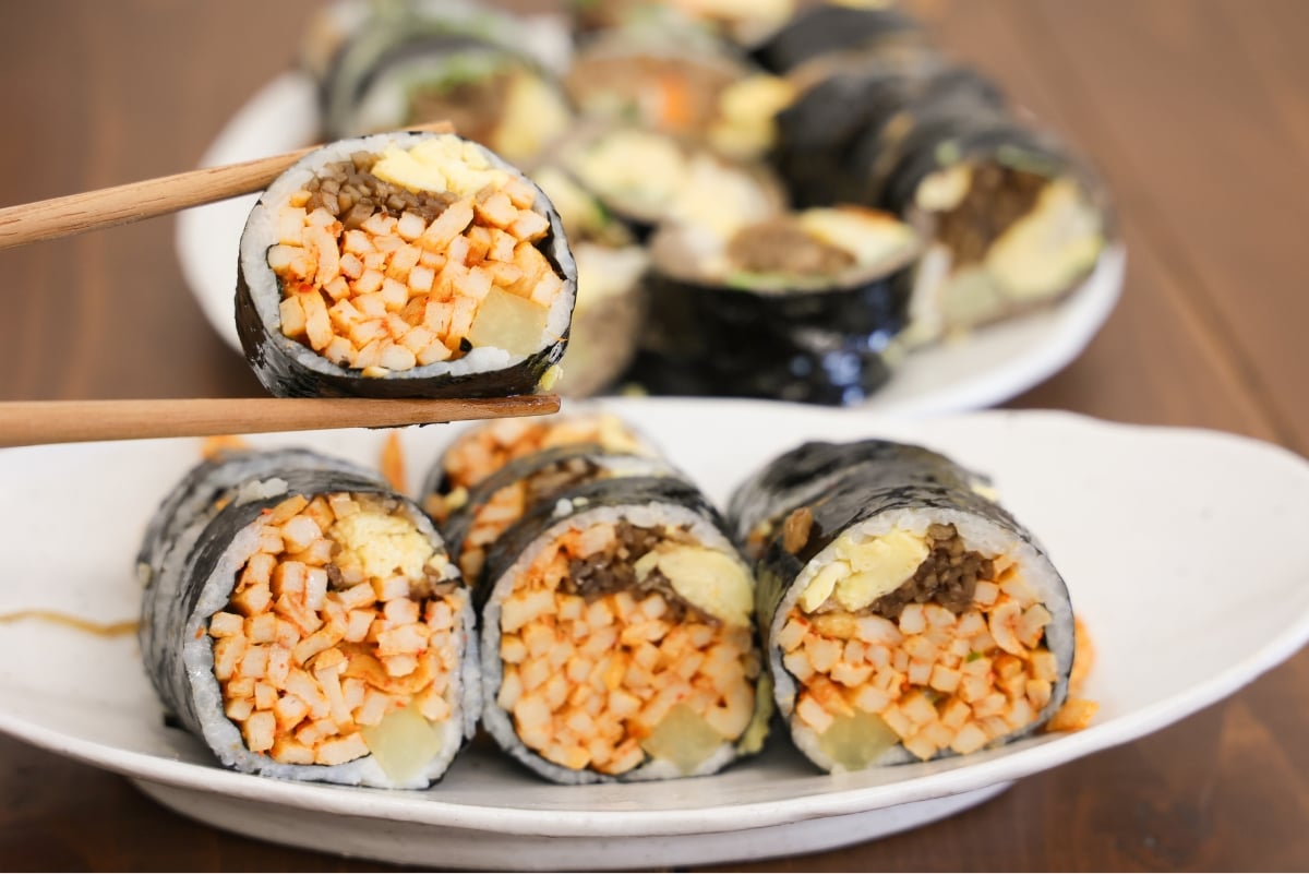 A spicy fishcake gimbap lifted with chopsticks