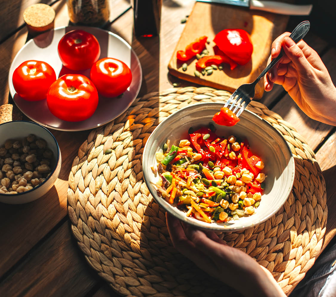 Young woman eating healthy food sitting in the beautiful interior with green flowers on the background